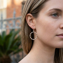Close-up of a woman wearing silver hoop earrings with a blurred outdoor background