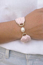 Bracelet with pink fabric charms and a pearl on a wrist against a white background