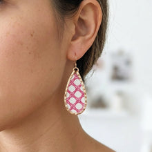 Close-up of a woman wearing a pink and gold teardrop earring with a blurred background.