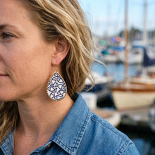 Woman wearing a blue and white patterned earring with boats in the background little fish print earring