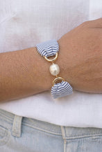 Bracelet with striped charms and a pearl bead on a wrist.