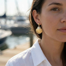 Close-up of a woman wearing gold shell earrings with a blurred background