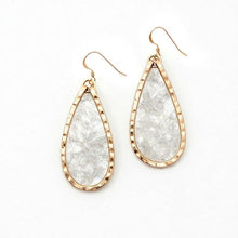 Teardrop-shaped earrings with gold frames and clear stone centers on a white background