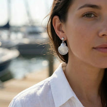 Close-up of a woman wearing shell-shaped earrings with a blurred background of boats.