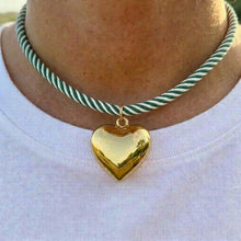 Gold heart pendant on a green and white striped cord necklace.