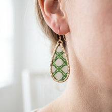 Teardrop-shaped earrings with green pattern worn by a person against a blurred background
