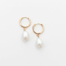 Gold hoop earrings with pearl drops on a light gray background