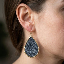 Teardrop-shaped earring worn by a person with a blurred background