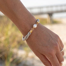 Bracelet with pearls and gold accents on a wrist against a blurred natural background