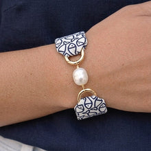 Bracelet with decorative charms and a pearl on a wrist against a dark shirt and light pants background.